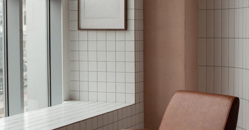 Small Apartment - Blank frame hanging on tiled wall near window in small light room with soft brown leather armchair on floor at home