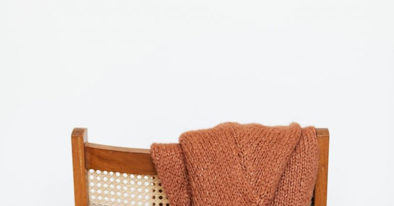 Storage Furniture - Brown coarse wool sweater hung on back of woooden chair against white wall